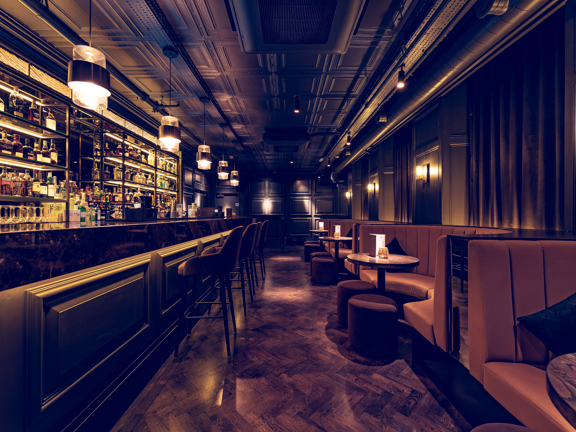 Long slim bar in Kong Glasgow, ambient lighting, velvet banquette seating and wooden panelled walls.  