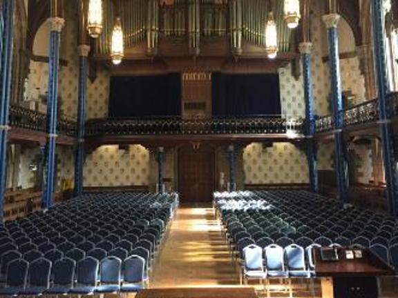 Grand room known as Bute Hall at University of Glasgow set up with rows of blue banqueting chairs. 