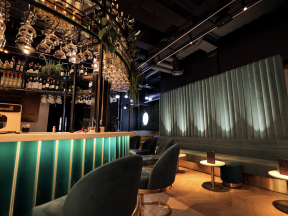 Bar with green tiles and green velvet chairs with white marble tables. 