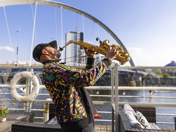 Man playing saxophone one the terrace next to riverside