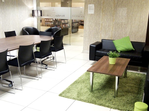 Room with long table surrounded by chairs and rug, sofa and coffee table on opposite. 