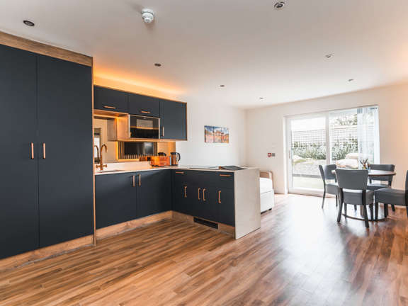 Open plan living, kitchen and dining area in a cottage with patio doors to the garden area. Contemporary style with black kitchen units, wooden floor and artwork. 