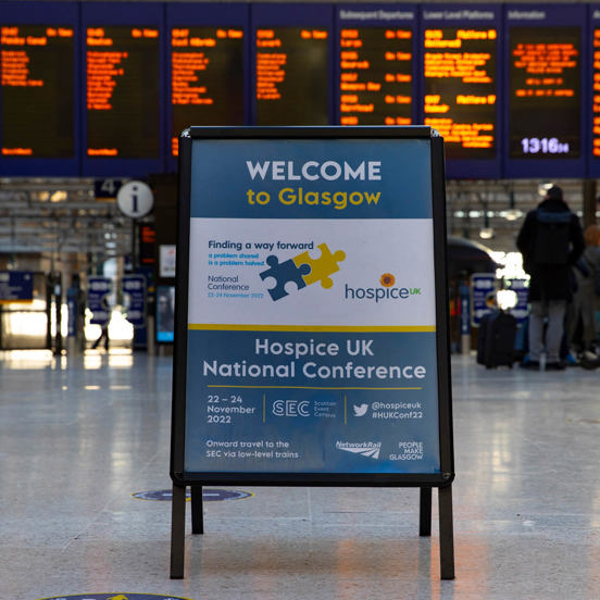 Large sign reading Welcome to Glasgow with a train station electronic board in the background