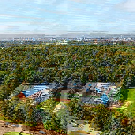 Aerial view of the Burrell Collection in Pollok Country Park, Glasgow, surrounded by woodland and open green space with the city skyline in the distance.