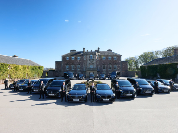 Fleet of black cars and peoples carriers outside a stately home