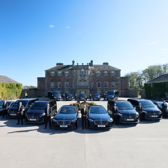 Fleet of black cars and peoples carriers outside a stately home