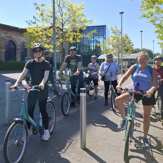 Smiling delegates, on bikes, stopped for a photo at the Clydeside Distillery in Glasgow, on a sunny day.