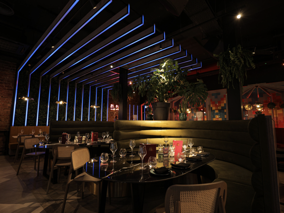 Restaurant with various tables and chairs. Neon blue lights line up across the wall and ceiling.