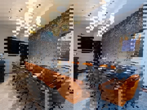 Hotel meeting room at Radisson Blu set up boardroom style with a large glass and metal table and tan leather chairs. 