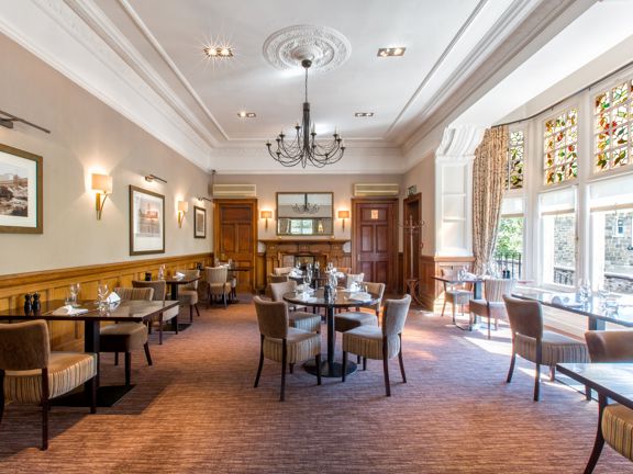 Hotel dining room with multiple tables and chairs, wood panelled walls and large stained glass window