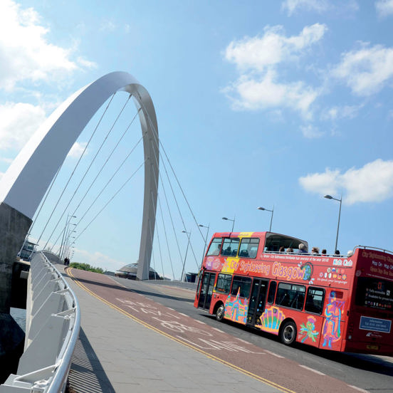 Red open-top double decker tourist bus reading City Sightseeing Glasgow on the side, crossing the steep Squinty bridge